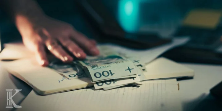 Dłoń układa banknoty 100 zł na otwartym notesie.