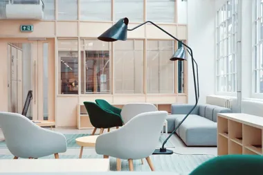 Jasny salon z szarą sofą, fotelami, stolikami i dużą czarną lampą stojącą.