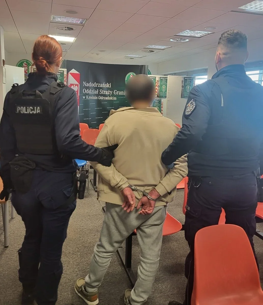 Funkcjonariusze policji i Straży Granicznej prowadzą zatrzymanego w kajdankach mężczyznę w pomieszczeniu Nadodrzańskiego Oddziału Straży Granicznej w Krośnie Od