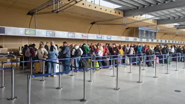 Pasażerowie czekają w kolejce do stanowisk odprawy na lotnisku.