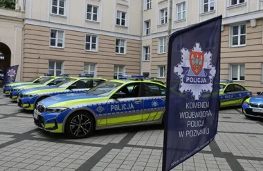 Policyjne radiowozy BMW oznakowane „Policja” stoją na brukowanym dziedzińcu przed budynkiem Komendy Wojewódzkiej Policji w Poznaniu.