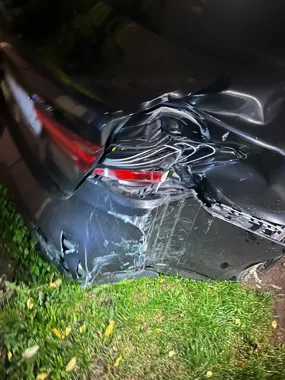 Uszkodzony tył ciemnego samochodu osobowego stojącego na trawniku przy drodze, nocą.