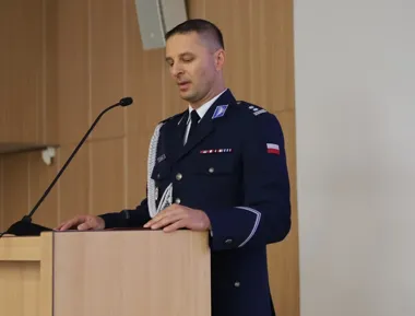 Funkcjonariusz w granatowym mundurze z biało-czerwoną flagą na rękawie przemawia z drewnianej mównicy w sali konferencyjnej.