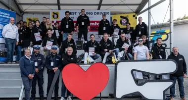 Grupa uczestników i organizatorów konkursu Best Young Driver pozuje do wspólnego zdjęcia na podium.