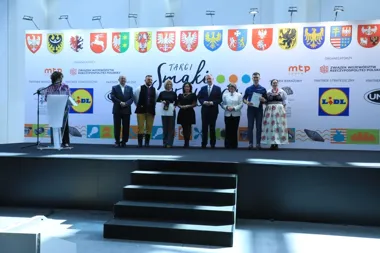 Grupa osób stoi na scenie podczas uroczystości na targach smaków, w tle baner z herbami województw i logotypami sponsorów.