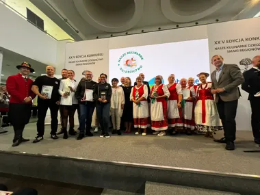 Grupa osób, w tym kucharze i kobiety w strojach ludowych, pozuje na scenie podczas uroczystości wręczenia nagród w konkursie kulinarnego dziedzictwa regionalneg